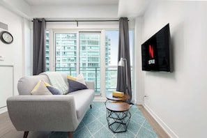 Ein modernes Wohnzimmer mit Sofa, Couchtisch, Flachbildfernseher und einem großen Fenster mit Blick auf die Stadt.