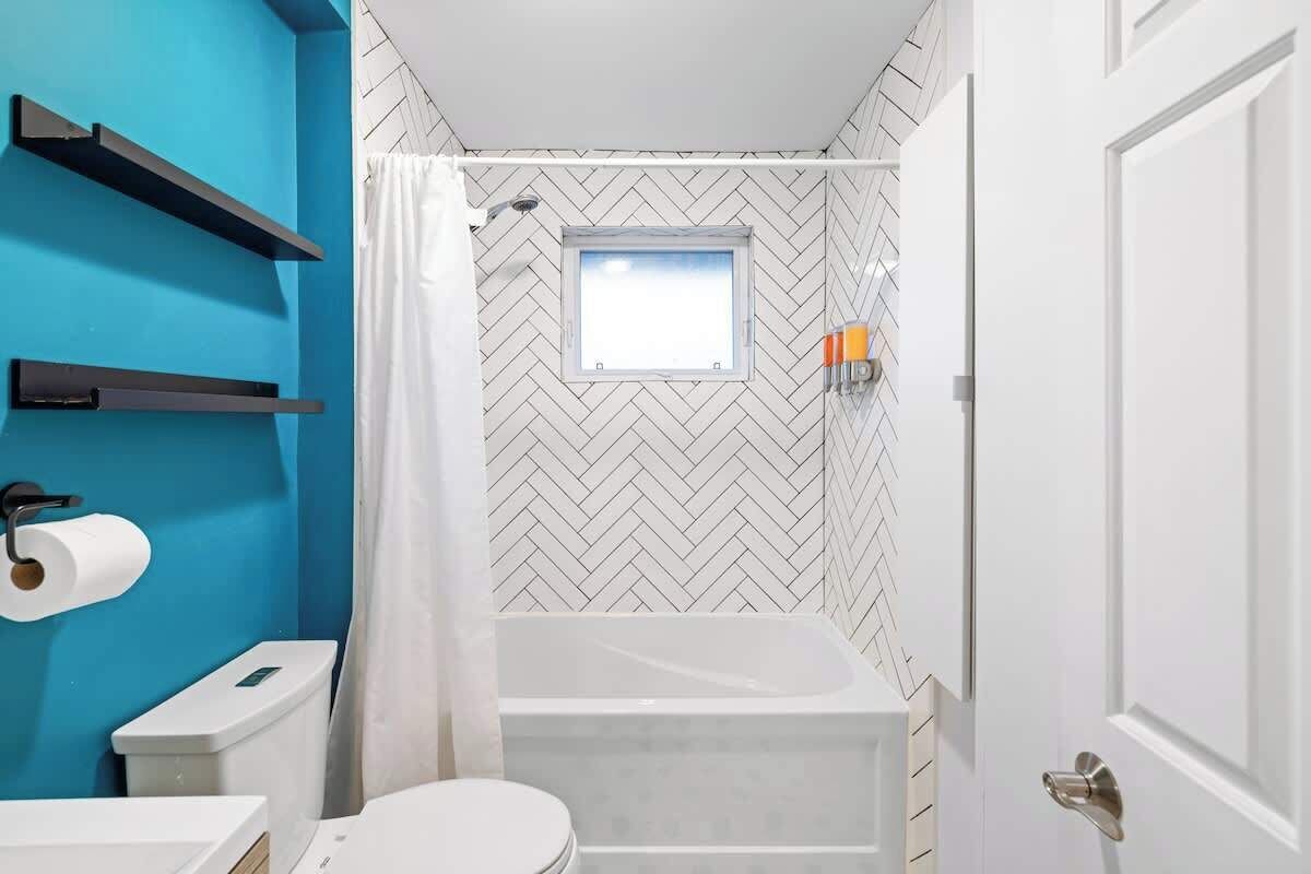 A bathroom with a herringbone patterned wall, a bathtub, a toilet, and a window.