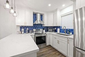 A modern kitchen with white cabinets, a stainless steel range hood, a microwave, and a refrigerator.