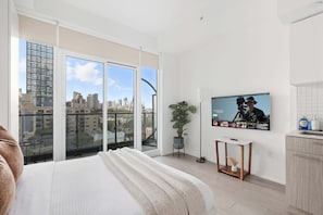 A modern apartment with a large balcony, a TV mounted on the wall, and a minimalist kitchen area. - Coffee Mornings & City Skylines, Toronto Studio! (Toronto)