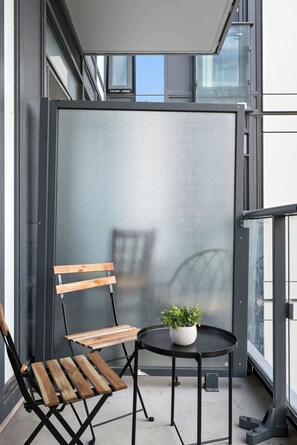 A balcony with a wooden chair, a small round table, and a potted plant. - Coffee Mornings & City Skylines, Toronto Studio! | Parking Available (Toronto)