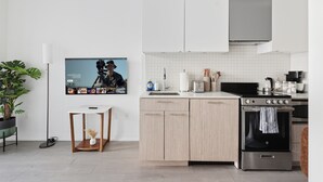 Uma cozinha moderna com armários brancos, fogão de aço inoxidável e uma televisão de tela plana na parede.