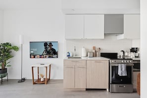 A modern kitchen with white cabinets, a stainless steel stove, and a flat-screen TV mounted on the wall. - Coffee Mornings & City Skylines, Toronto Studio! (Toronto)