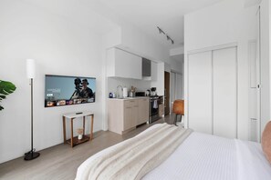 A modern hotel room with a large bed, a flat-screen TV mounted on the wall, a small table, and a kitchen area in the background. - Coffee Mornings & City Skylines, Toronto Studio! | Parking Available (Toronto)