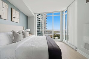 A bedroom with a large bed, a view of a building through a glass door, and a window with a view of the sky. - Luxury 2BR Condo with King Beds & Views (Toronto)