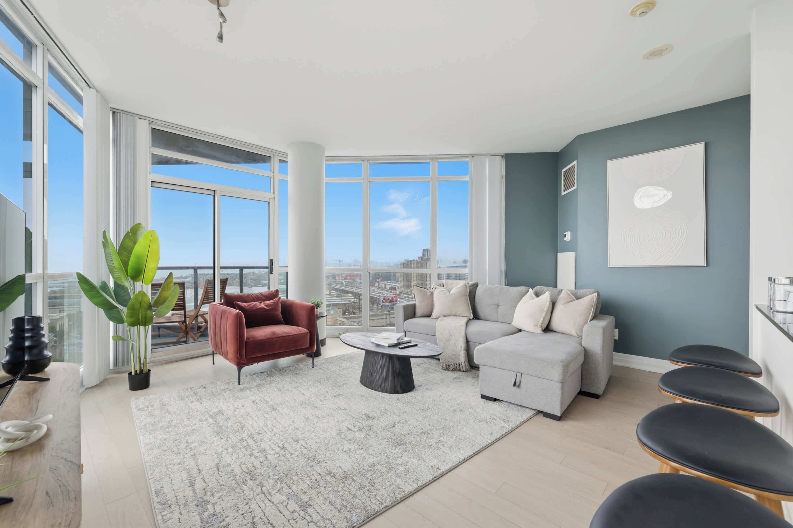 A modern living room with a large window, a red armchair, a grey sofa, and a coffee table.