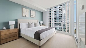 Une chambre moderne avec un grand lit, des tables de chevet et une vue sur un immeuble de grande hauteur.