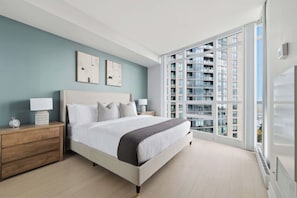 Ein modernes Schlafzimmer mit einem großen Bett, Nachttischen und Blick auf ein Hochhaus.