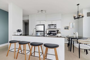 Una cocina moderna con una isla central, taburetes de bar, una mesa de comedor con sillas y una araña.