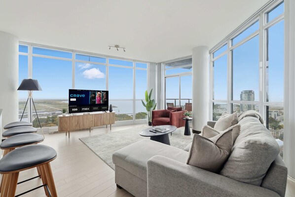 A spacious living room with a large TV, comfortable seating, and a view of the city. - Luxury 2BR Condo with King Beds & Views (Toronto)