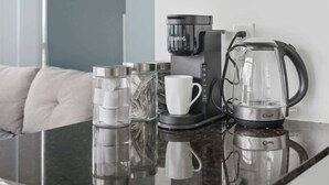 Une chambre d’hôtel moderne avec une machine à café noire, une cafetière en verre et une tasse blanche posée sur une surface réfléchissante.
