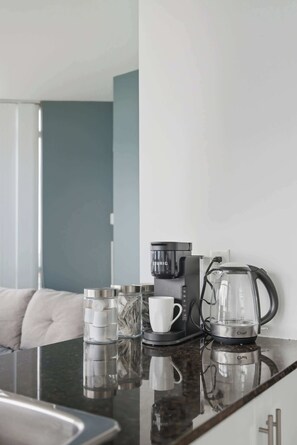 Ein modernes Hotelzimmer mit einer schwarzen Kaffeemaschine, einer Glas-Kaffeekanne und einer weißen Tasse auf einer spiegelnden Oberfläche.