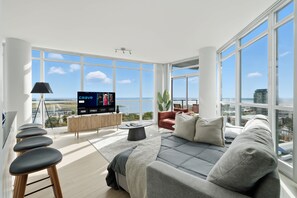 A modern living room with a large TV, a sofa, a coffee table, and a view of the city and water. - Luxury 2BR Condo with King Beds & Views | Parking Available (Toronto)