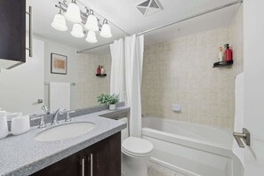 A modern bathroom with a granite countertop, a white sink, a mirror, and a shower area. - Luxury 2BR Condo with King Beds & Views (Toronto)