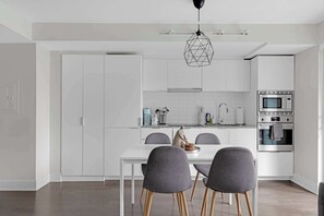Una cocina moderna con armarios blancos, una mesa de comedor con sillas y un horno empotrado.