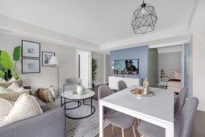 Una sala de estar moderna con un sofá gris, una mesa de centro y un comedor con una mesa blanca y sillas grises.