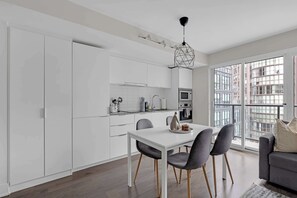Une cuisine moderne avec des meubles blancs, une table à manger avec des chaises et une grande fenêtre donnant sur la ville.