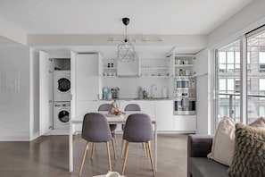 Eine moderne Küche mit integrierten Geräten, ein Essbereich mit grauen Stühlen und ein großes Fenster, das für natürliches Licht sorgt.