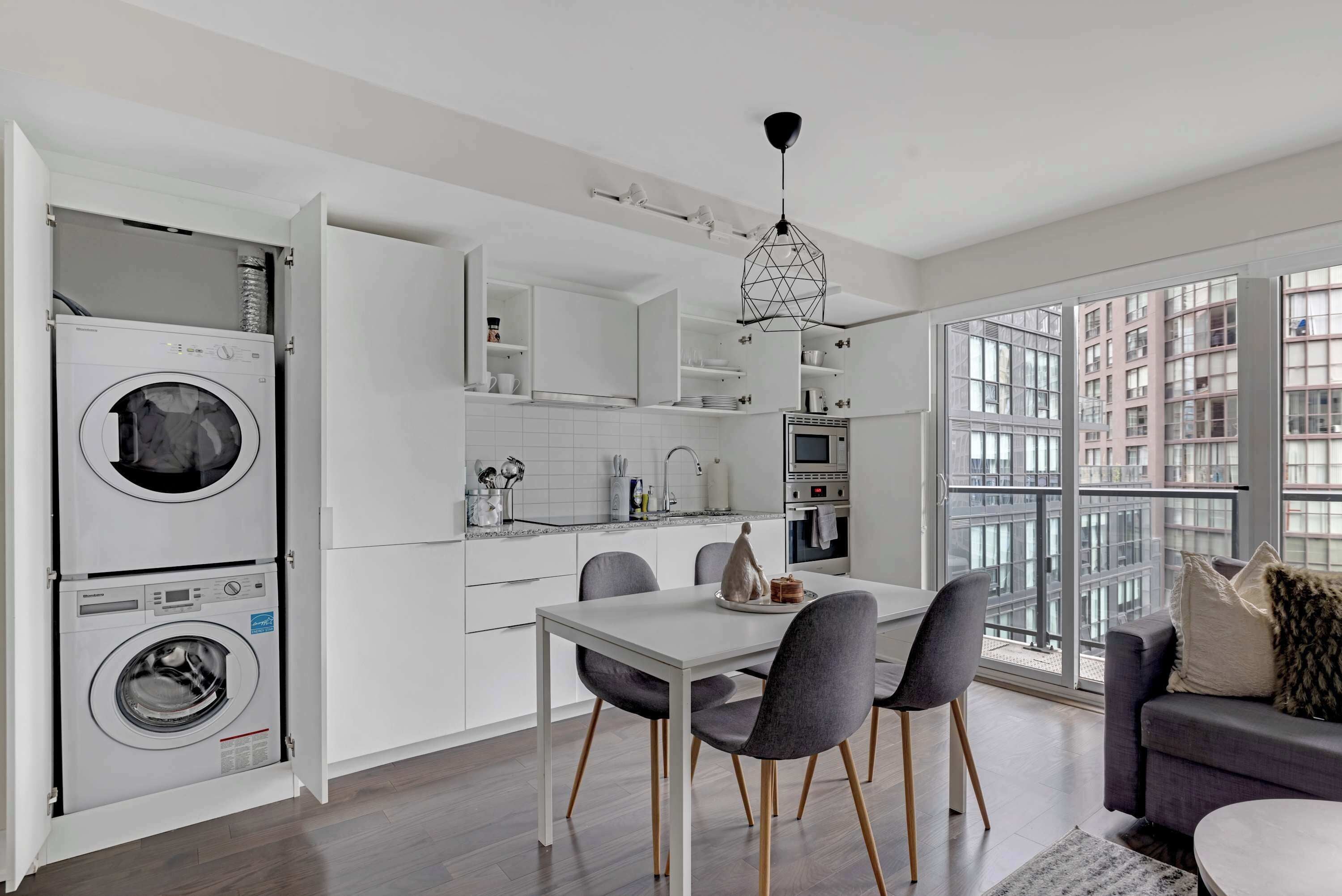 Een moderne keuken met inbouwapparatuur, een eethoek met een tafel en stoelen, en een stadszicht door grote ramen.