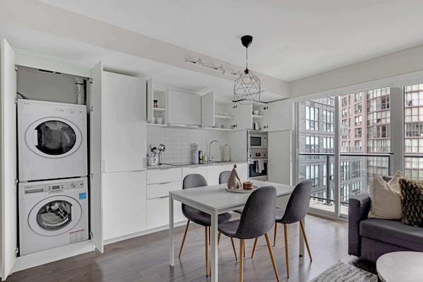 Una cocina moderna con electrodomésticos integrados, una zona de comedor con mesa y sillas, y vistas a la ciudad a través de amplias ventanas.