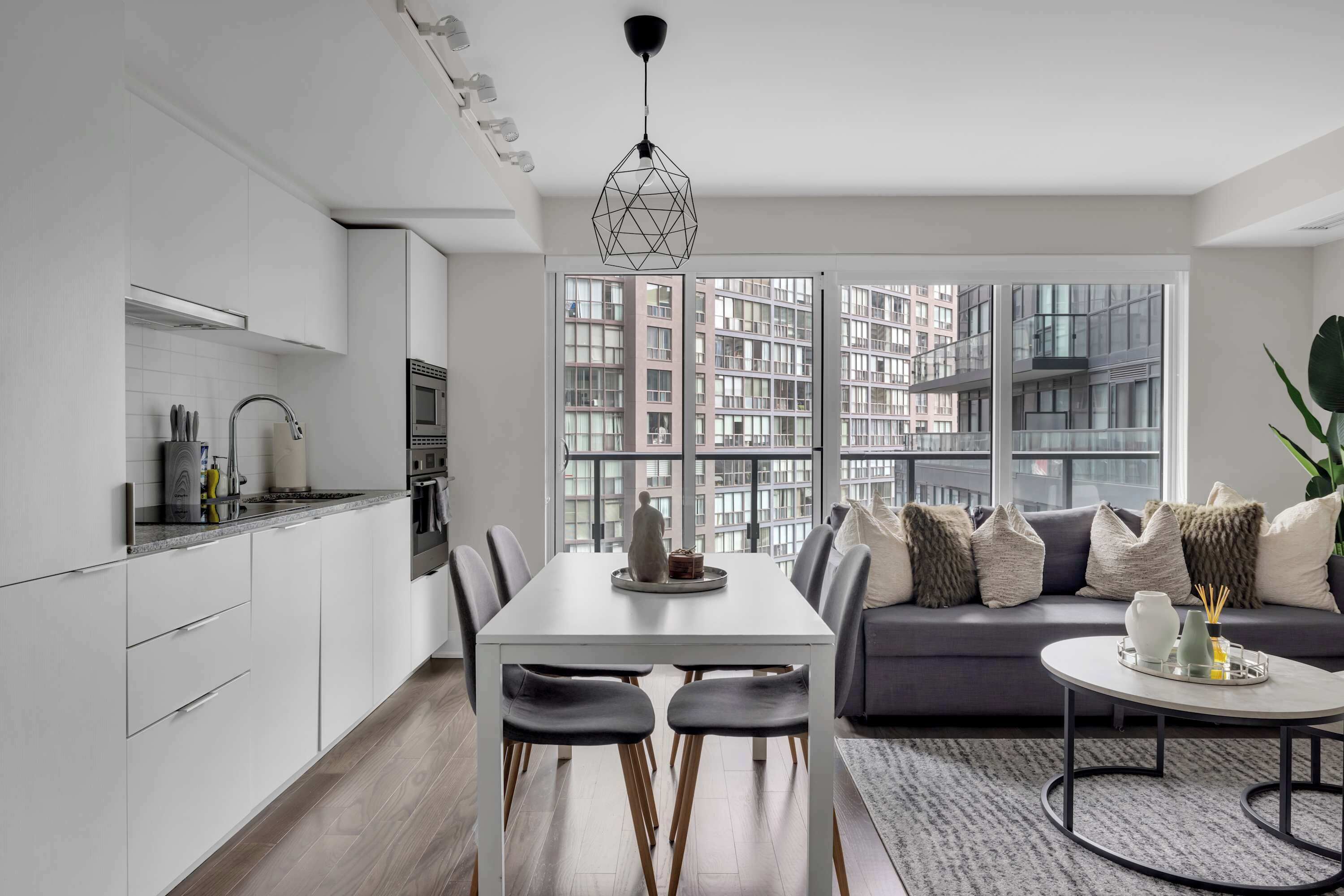 A modern kitchen with white cabinetry, a dining area with a white table, and a gray sofa with multiple cushions.