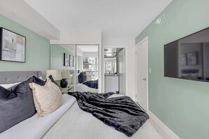 A bedroom with a bed, a TV, a mirror, and a view of the outside. - Financial District 2BR Condo, 55" TV, Free Parking (Toronto)