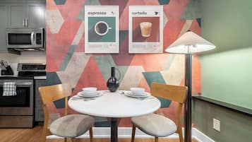 Un coin repas avec une table ronde, deux chaises, un vase et une lampe. Deux tableaux encadrés sont accrochés au mur.