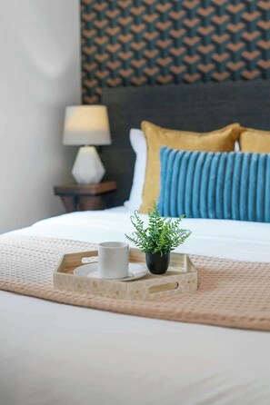 A neatly made bed with a white duvet, a blue pillow, and a yellow accent pillow. There is a small potted plant on a tray beside the bed, and a white mug on the tray. - Sleek Downtown Toronto Stay, Cafes, Shops Nearby | Parking Available (Toronto)
