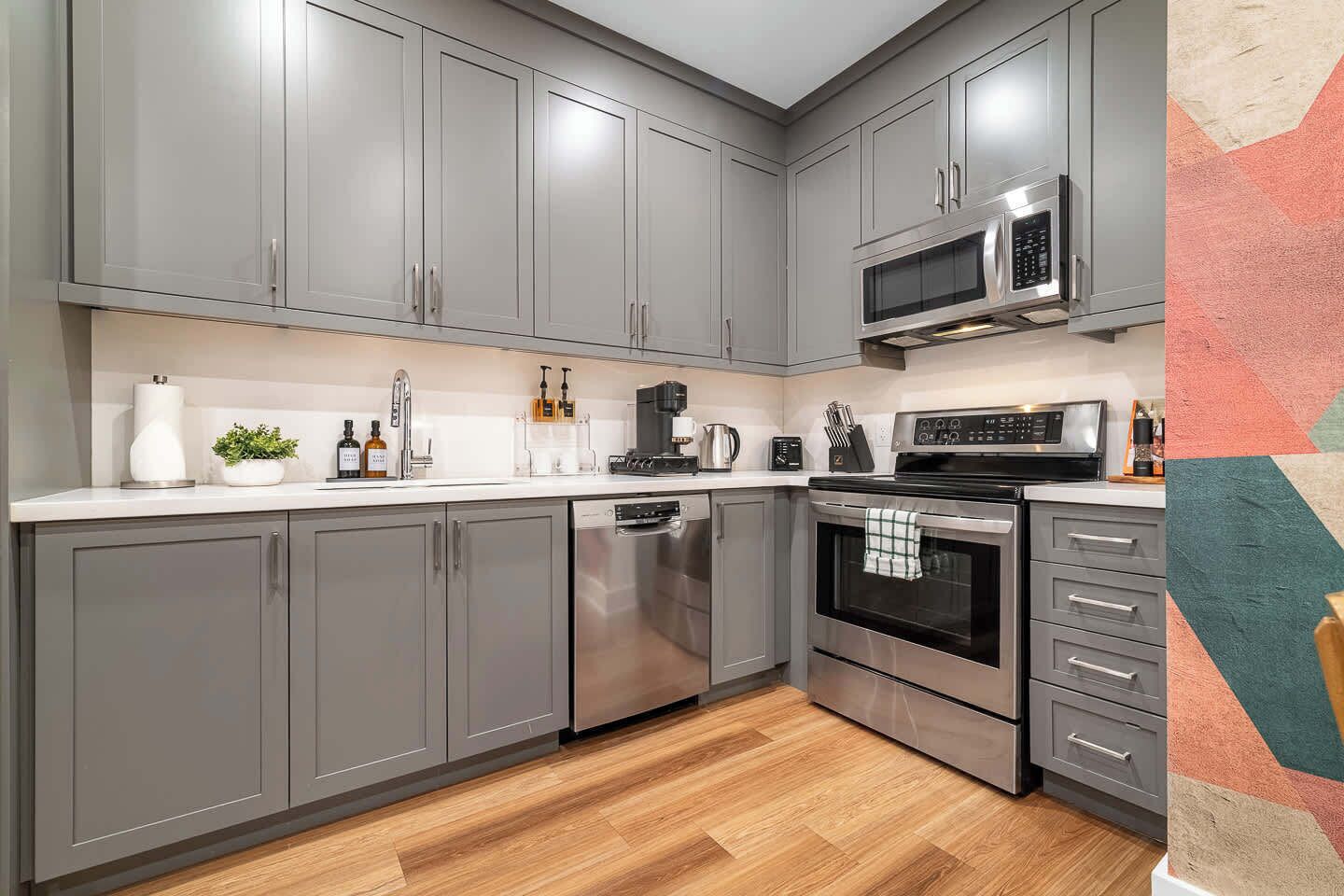 A modern kitchen with grey cabinetry, stainless steel appliances, and a wooden floor.