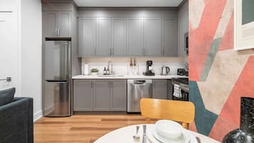 Une cuisine moderne avec des meubles gris, un réfrigérateur en acier inoxydable et un coin repas doté d’une table ronde.