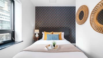 Une chambre d’hôtel avec un lit, une fenêtre, un miroir fixé au mur et un papier peint à motifs.