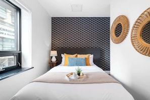 Ein Hotelzimmer mit Bett, Fenster, Wandspiegel und einer Wand mit Muster.