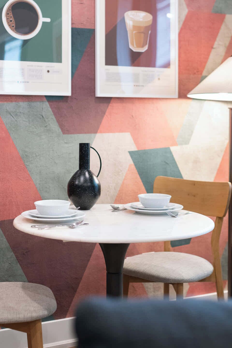 A dining table with a black vase, white plates, and a wooden chair.