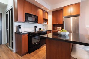 A modern kitchen with wooden cabinets, a stainless steel refrigerator, a black microwave, and a coffee maker. - Elegant 2BR Condo in Prime Downtown Location | Parking Available (Toronto)