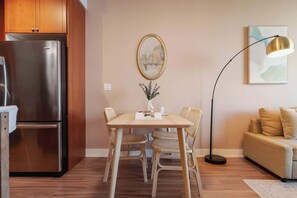 A modern kitchen with a stainless steel refrigerator, a dining table with wicker chairs, a vase with greenery, and a floor lamp. - Elegant 2BR Condo in Prime Downtown Location | Parking Available (Toronto)