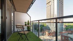 Un balcon avec une petite table et des chaises, un pot de fleurs et une vue sur le paysage urbain, avec ses bâtiments.