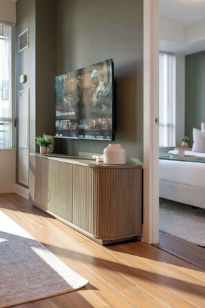 Ein modernes Wohnzimmer mit einem großen Flachbildfernseher, der an einem Holzschrank befestigt ist, einem weißen Sofa und einem kleinen Blumentopf.
