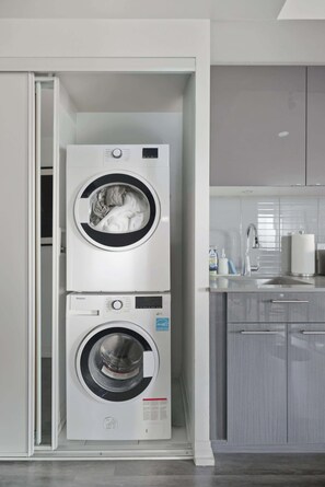 A compact, modern laundry room with two stacked washing machines and a built-in sink. - Downtown Core 1BR Condo with Balcony | Walk to TMU (Toronto)