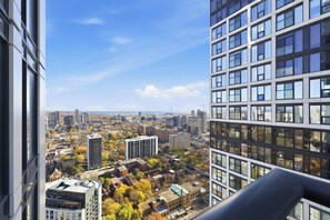 A high-rise building with multiple floors, large windows, and a view of a cityscape with various buildings and trees. - Downtown Toronto 1BR | Skyline Balcony (Toronto)