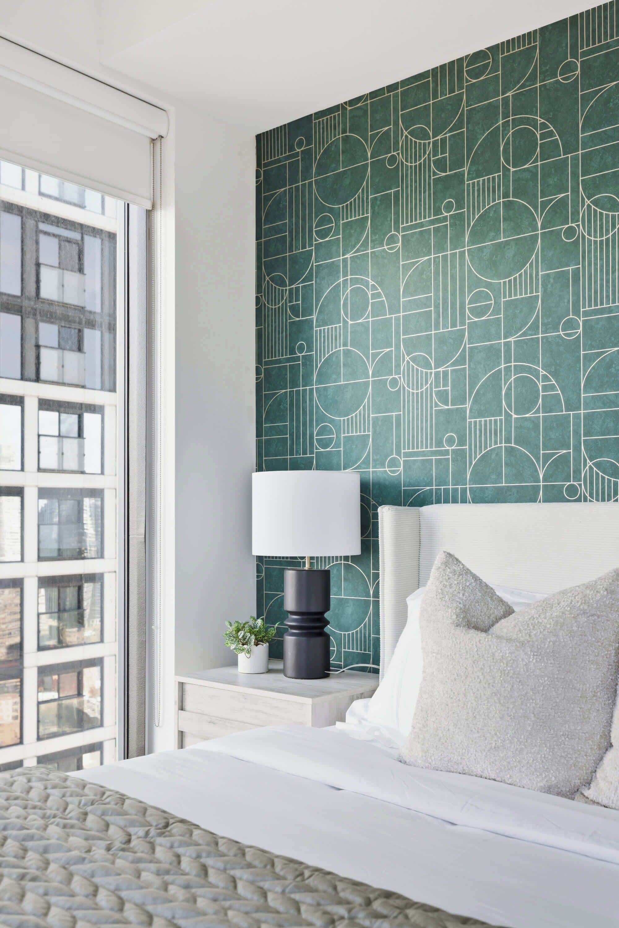 A bedroom with a bed, a nightstand, a lamp, and a window with a view of buildings.