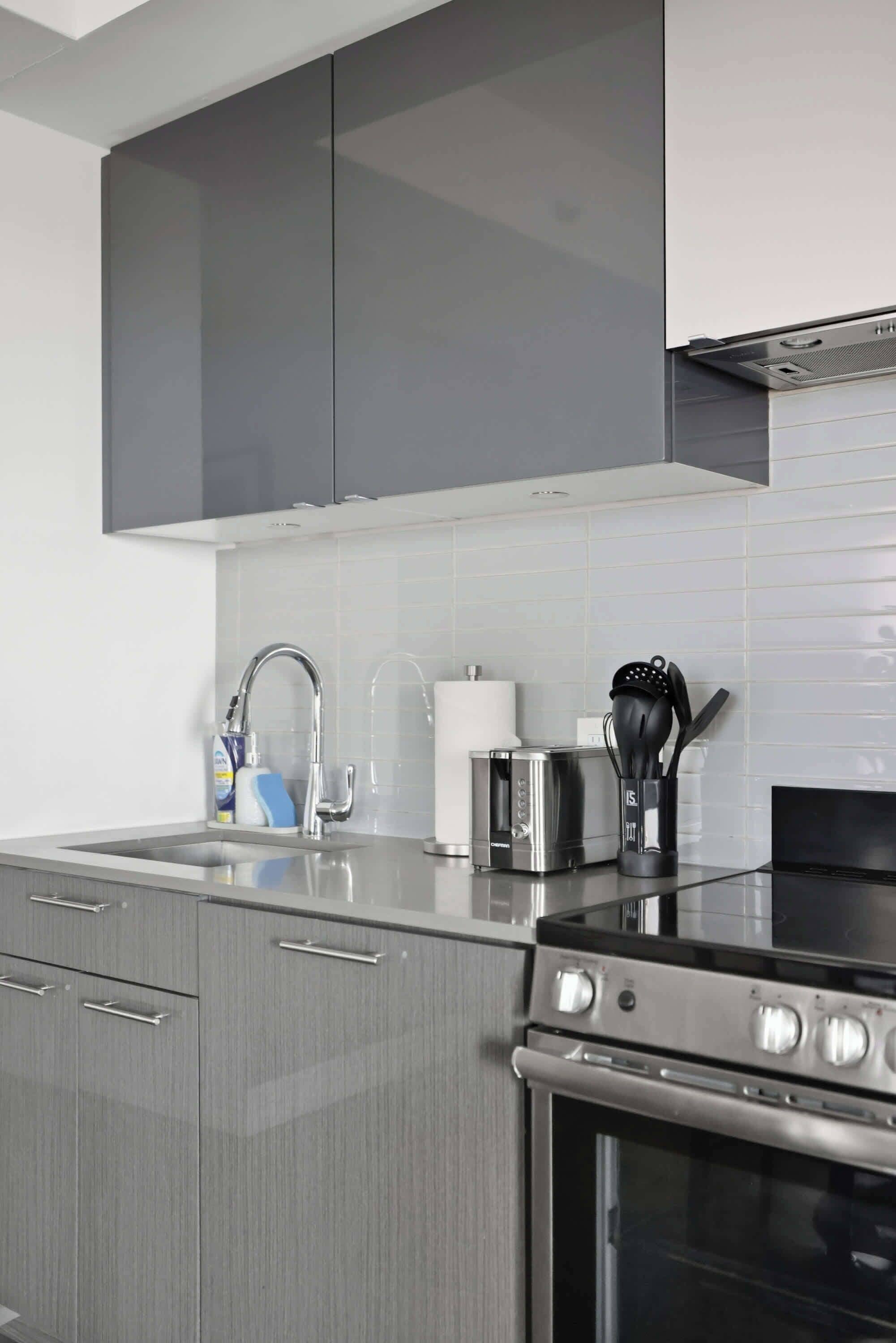 A modern kitchen with grey cabinetry, a stainless steel stove, a toaster, and a sink with a faucet.