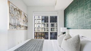 Een moderne hotelkamer met een groot bed, uitzicht op de stad door het raam, en een groene abstracte wand.