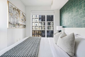 A modern hotel room with a large bed, a view of the city through the window, and a green abstract wall. - Downtown Core 1BR Condo with Balcony | Walk to TMU (Toronto)