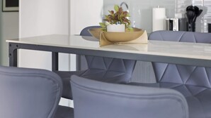 Een moderne keuken met grijze kastjes, een wit aanrecht en een eettafel met vier stoelen.