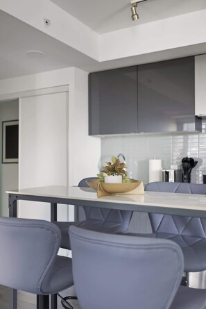 A modern kitchen with grey cabinets, a white countertop, and a dining table with four chairs. - Downtown Core 1BR Condo with Balcony | Walk to TMU (Toronto)