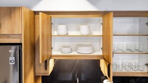 Una cucina con mobili in legno, un frigorifero in acciaio inossidabile ed scaffali con piatti e bicchieri bianchi.