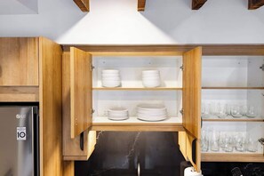 A kitchen with wooden cabinets, a stainless steel refrigerator, and shelves with white plates and glasses.