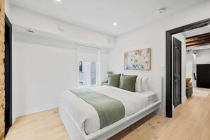 A bedroom with a bed, a painting, and a door leading to another room. - Parkdale 1BR Hideaway | Patio & Free Parking (Toronto)