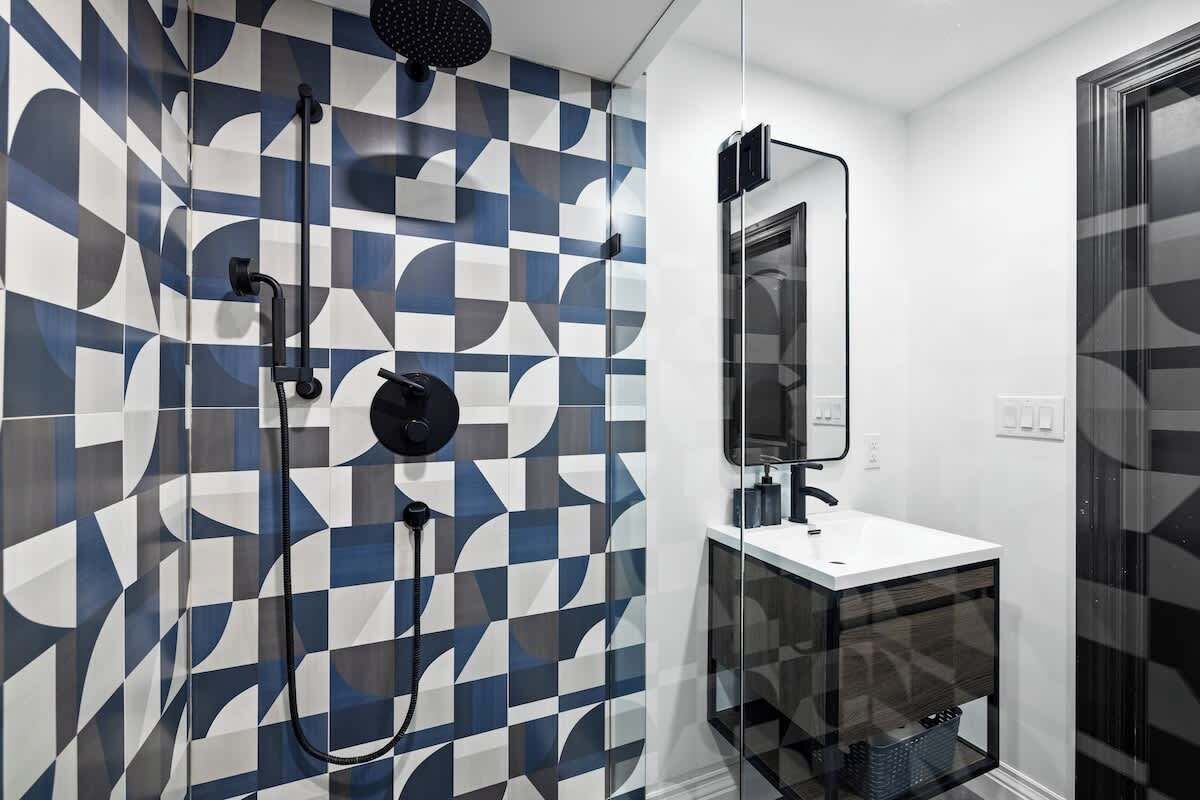 Une salle de bain moderne avec un carrelage aux motifs géométriques, une douche à parois de verre, un lavabo blanc et un miroir.