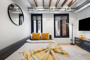 Une chambre à coucher avec un lit, deux fenêtres, un miroir et un téléviseur.